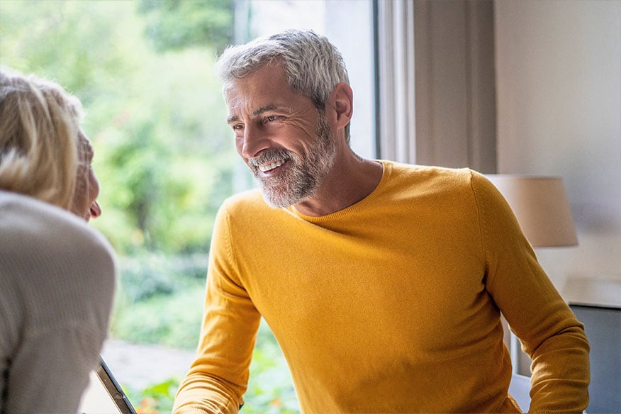 A person with gray hair and beard smiling in a yellow sweater